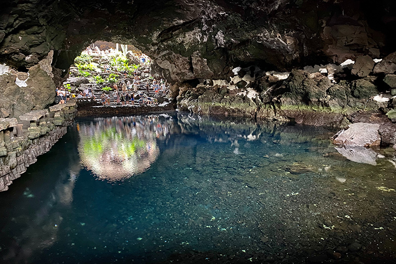 Reflection on the water inside a volcanic cave at Jameos del Agua, Lanzarote, with natural vegetation illuminated by daylight.