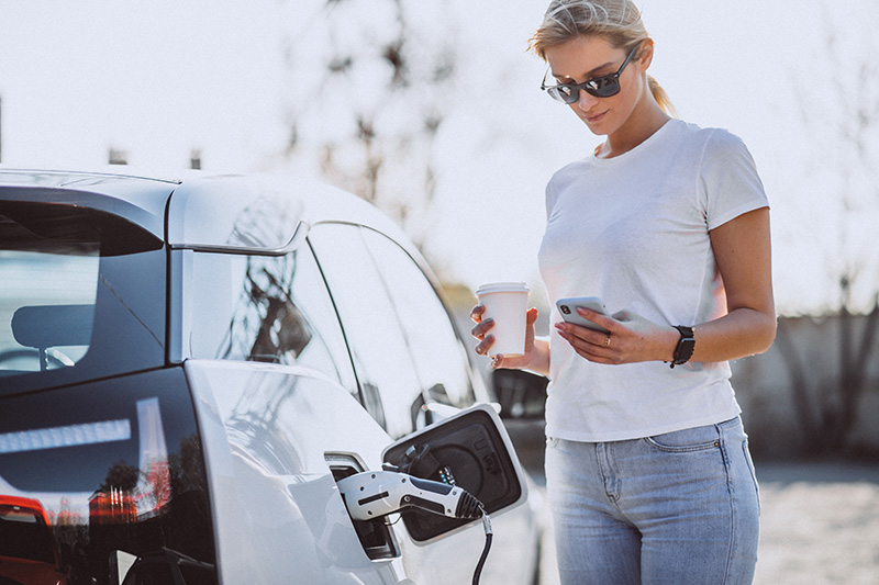 Frau lädt ein Elektroauto an einer Tankstelle auf