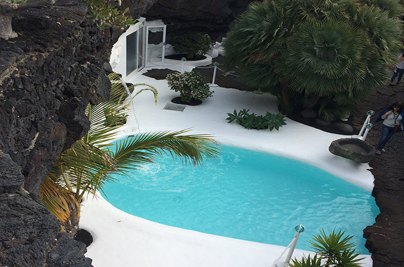 View of the César Manrique Foundation in Tahíche, Lanzarote, featuring its outdoor pool integrated into the volcanic landscape, with its signature white architecture surrounded by tropical vegetation.