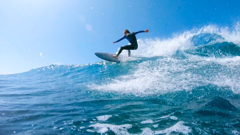 Surfeur réalisant une manœuvre sur une grande vague bleue sous un ciel ensoleillé à Fuerteventura.